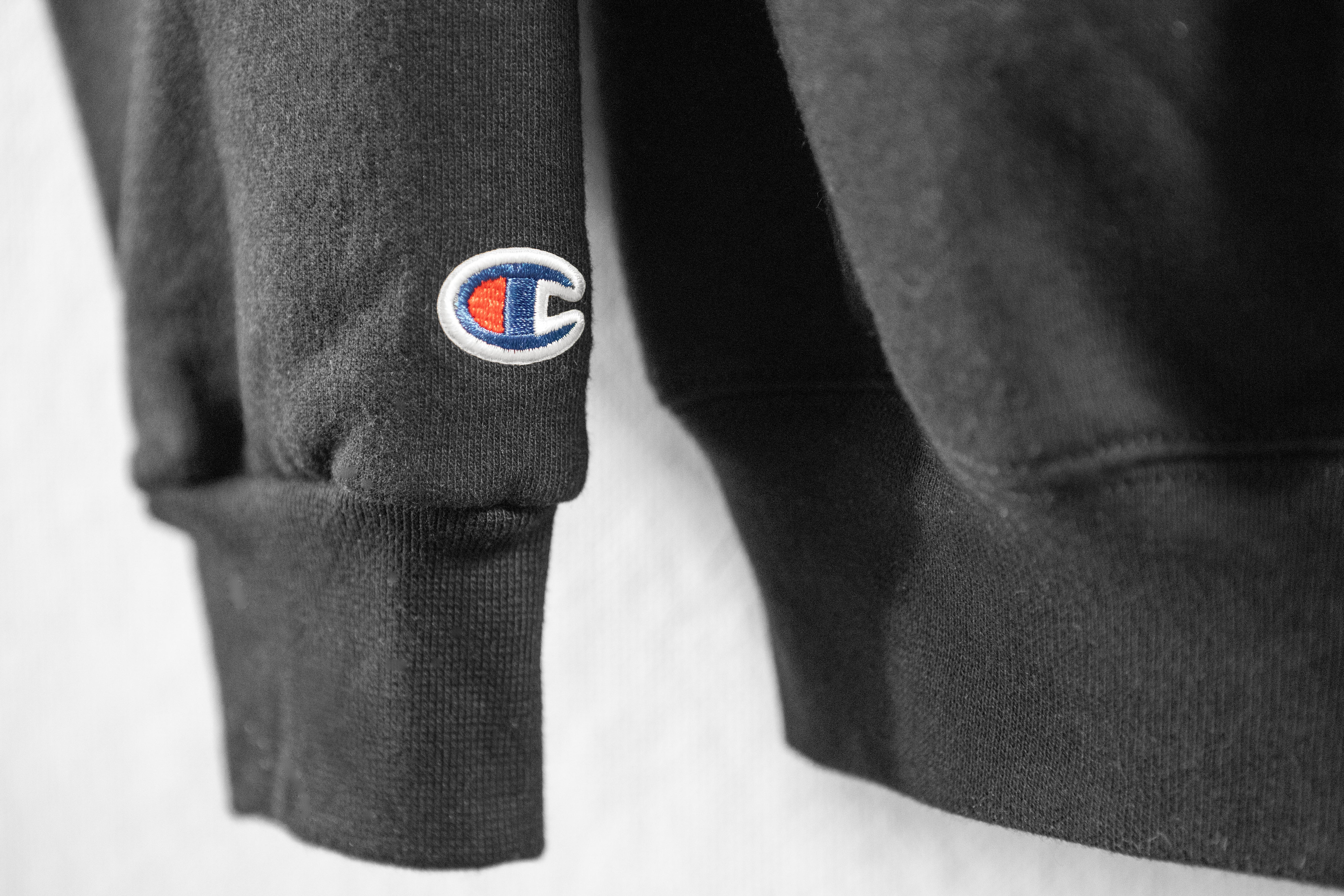 Close-up of a dark gray sweatshirt with a Champion logo on the sleeve against a white background